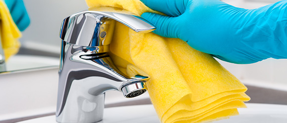 a person with a rubber glove cleaning a steel tap with a yellow cloth