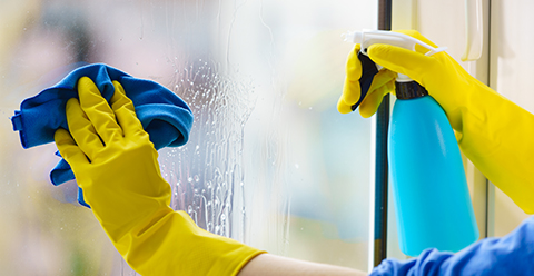 a person wearing yellow gloves using a spray and cloth to clean the inside of a window