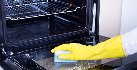 a person with yellow gloves using a sponge to clean the interior of an oven
